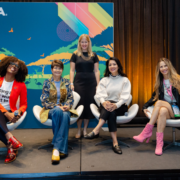 Diverse group of women pose onstage in front of a colorful IAAPA Expo backdrop during a panel on women in the entertainment industry.
