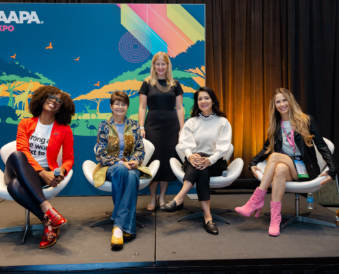 Diverse group of women pose onstage in front of a colorful IAAPA Expo backdrop during a panel on women in the entertainment industry.