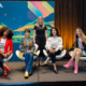 Diverse group of women pose onstage in front of a colorful IAAPA Expo backdrop during a panel on women in the entertainment industry.