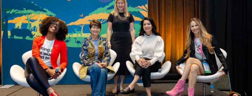 Diverse group of women pose onstage in front of a colorful IAAPA Expo backdrop during a panel on women in the entertainment industry.